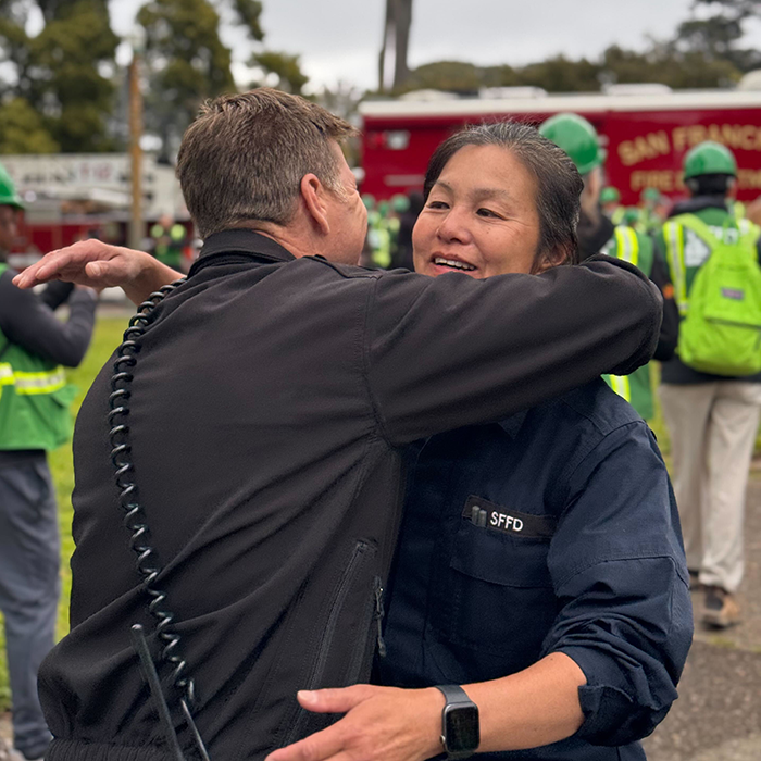 Two firefighters hug each other with big smiles.