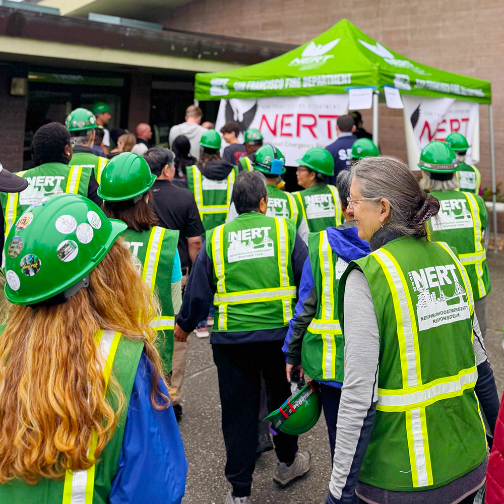 Dozens of N E R Ts with team vests and helmets on walk back into the San Francisco County Fair Building.