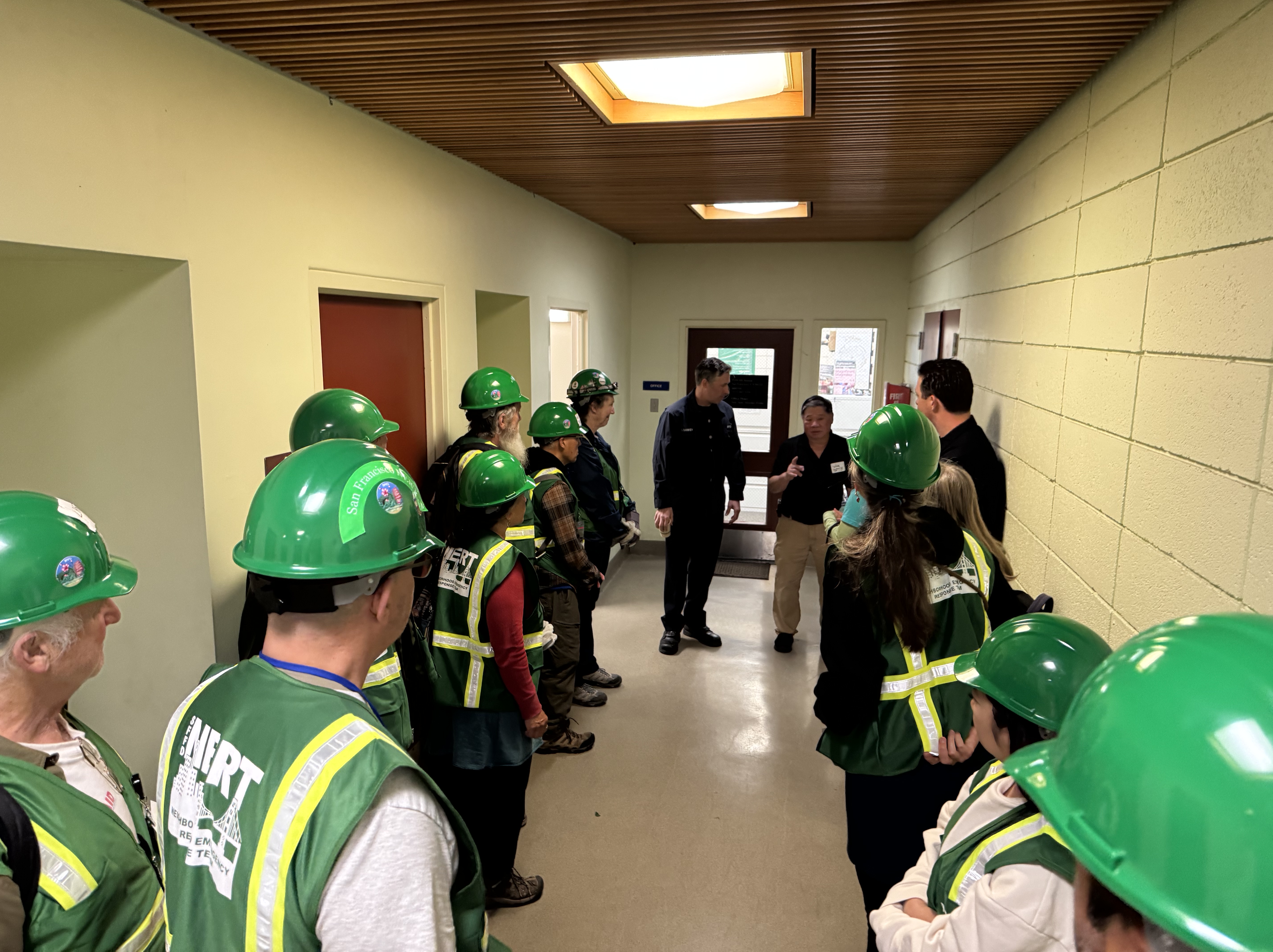 A group of N E R Ts standing in a hallway, listening to a facilitator and firefighter before entering the All Hazards room.