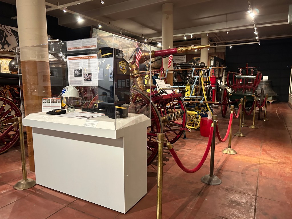 A scene in the S F F D museum showing a display case with a uniform and various horse-drawn wagons.
