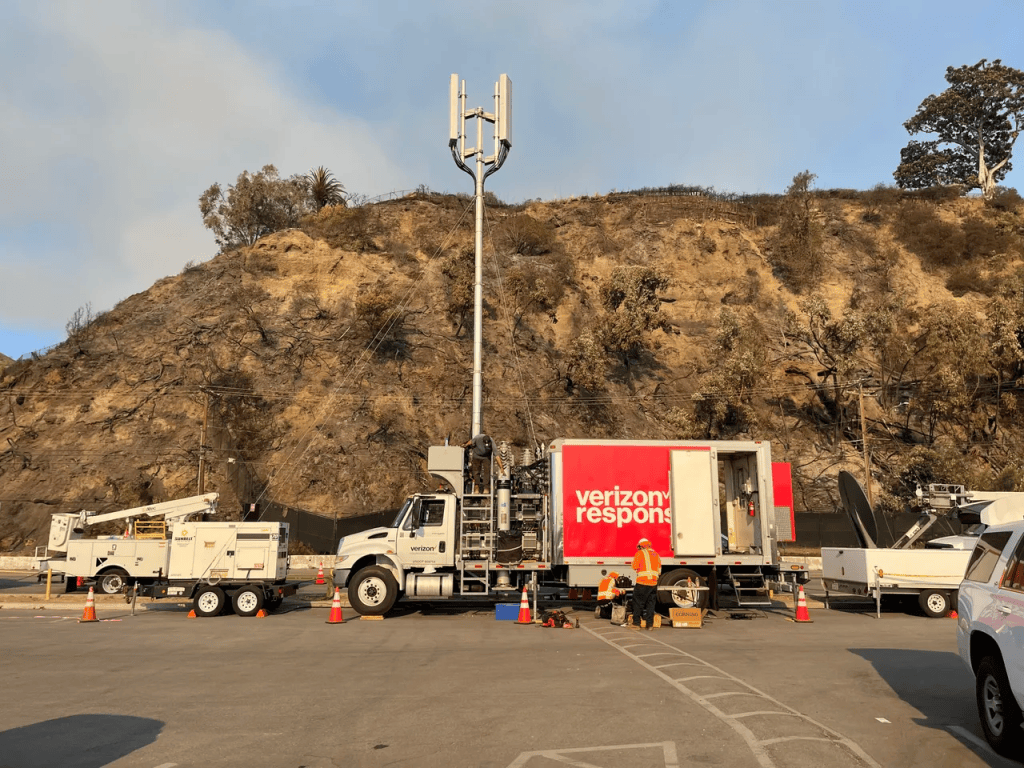 A large truck with a cellular telephone antenna mounted on it's roof, in a setting where there has been a wildfire.